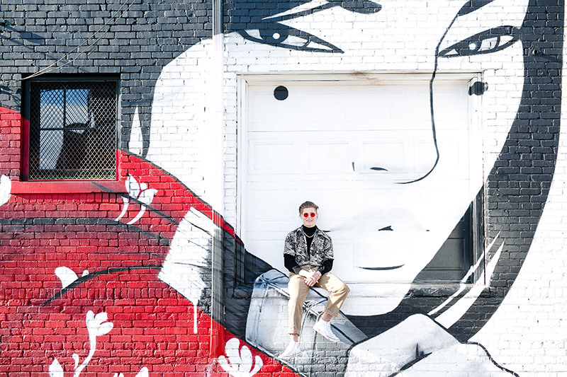 high school senior boy with red glass sitting by graffiti wall